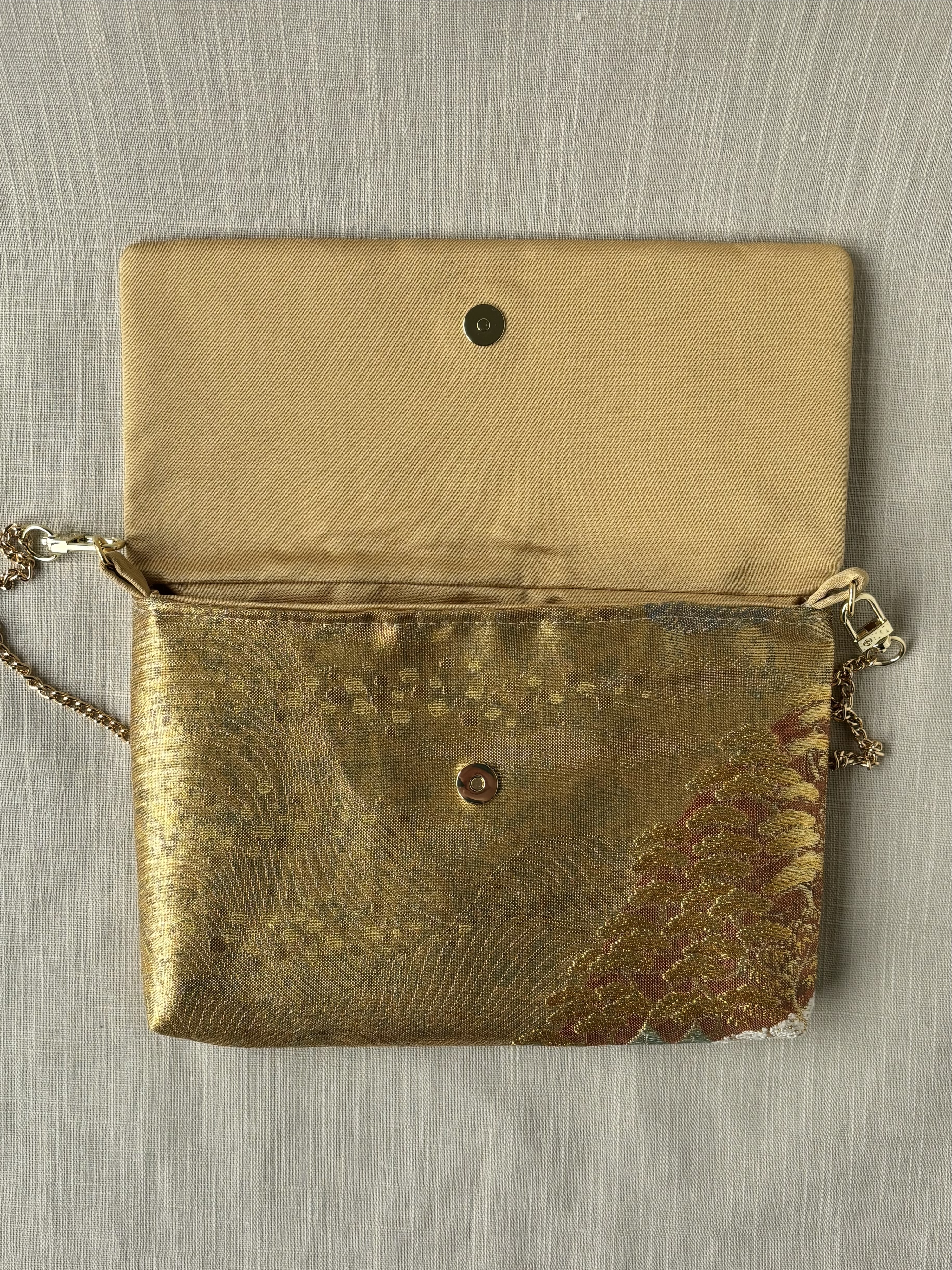 Overhead view of the clutch with open flap on a cream coloured textured linen background, showing the interior lining of a soft golden silk.